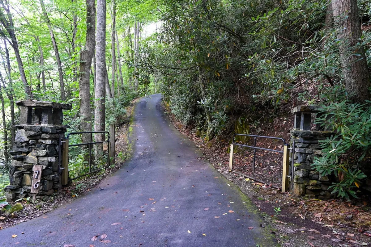 This image depicts the stone gate pillars and a winding road flanked by lush greenery, giving a sense of arrival and seclusion. The tranquil setting hints at spacious grounds perfect for children to explore safely while parents relax.