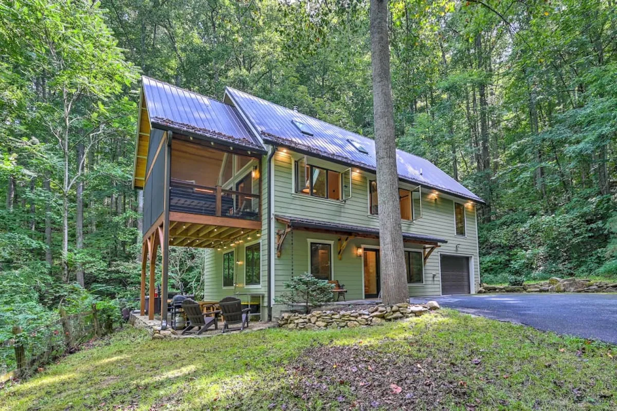 A modern wooden deck surrounded by tall trees, set up for outdoor dining or relaxing. The architecture blends with the natural environment, and the deck is positioned to allow for both shade and dappled sunlight, embodying the spirit of bringing the outdoors in.