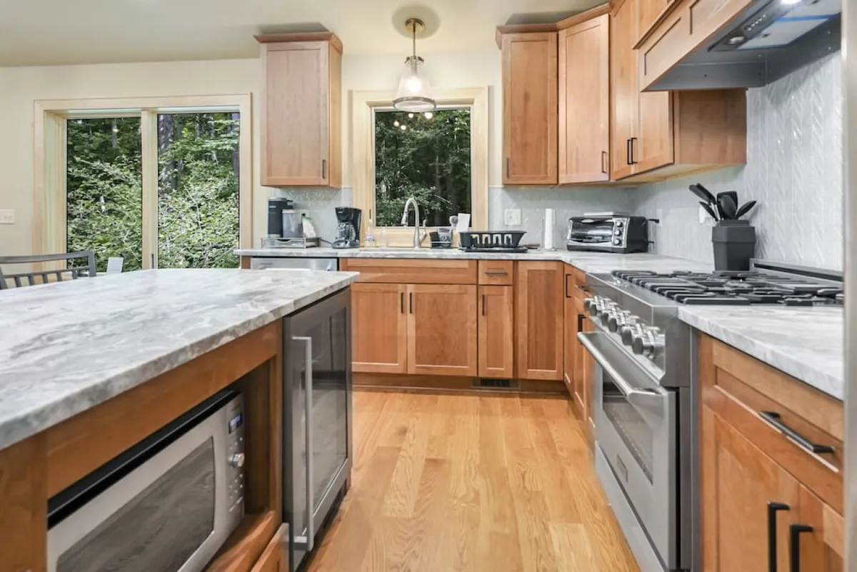 A warm, inviting kitchen featuring a central island perfect for meal prep or gathering around. The space is highlighted by stainless steel appliances, wooden cabinetry, and a sink with a window view, creating a functional yet homey atmosphere ideal for culinary adventures and social cooking.