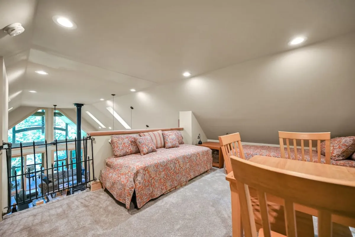 A bright, airy room with a comfortable sofa featuring patterned cushions, a wooden dining table ready for gatherings, and generous windows letting in ample natural light. The view through the windows showcases the tranquil forest, while the blend of seating arrangements supports both socializing and quiet moments.