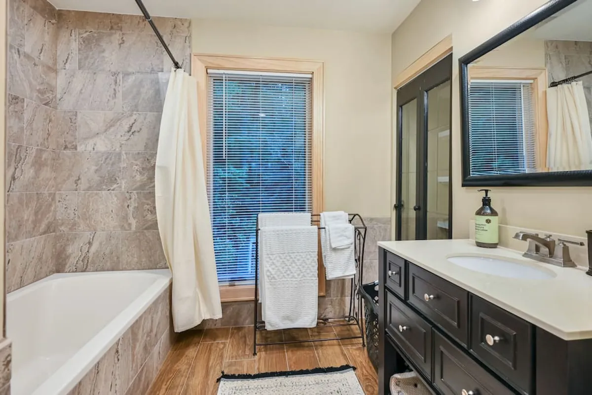 A tranquil bathroom featuring a standalone bathtub, vanity with mirror, window for natural light, and neatly arranged towels. The space feels bright, soothing, and designed for rejuvenation after a long day of adventure.