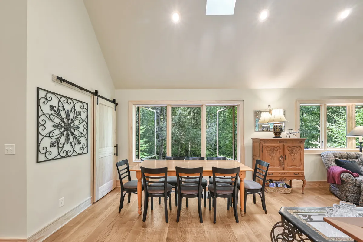 A cozy dining area with a large table, wooden cabinet, decorative wall art, and expansive windows. The setup is perfect for intimate family dinners, social games, and holiday gatherings, with plenty of natural light contributing to an inviting ambiance.