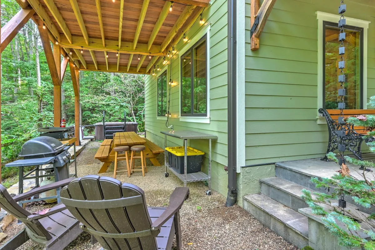 A spacious wooden deck featuring a grill, outdoor dining table, and comfortable seating, all nestled among vibrant greenery. The deck is set for casual meals, barbecues, or morning coffee, providing a clear view of the surrounding natural beauty.
